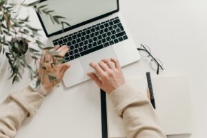 Person sitzt am Schreibtisch und tippt am Laptop