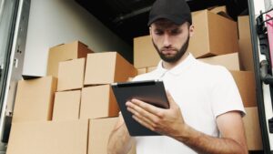 Mann mit Tablet vor Transporterkofferraum voller Pakete
